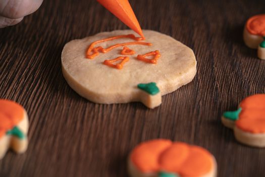 Close up of decorating cute Halloween pumpkin gingerbread cookies with frosting icing cream topping bag.