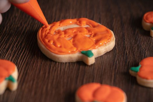 Close up of decorating cute Halloween pumpkin gingerbread cookies with frosting icing cream topping bag.