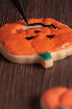 Close up of decorating cute Halloween pumpkin gingerbread cookies with frosting icing cream topping bag.