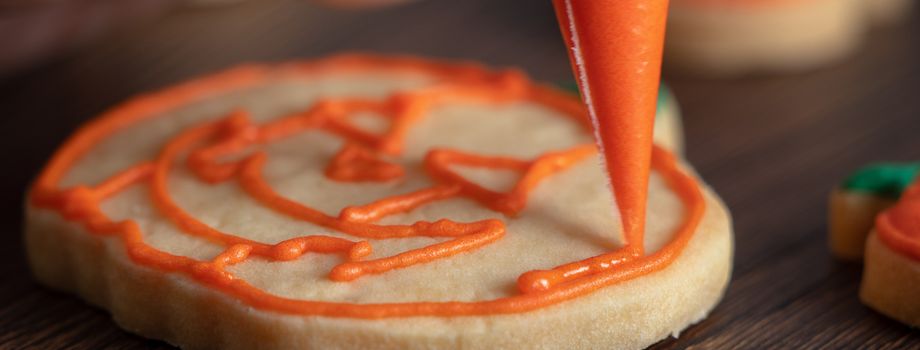 Close up of decorating cute Halloween pumpkin gingerbread cookies with frosting icing cream topping bag.