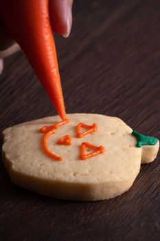 Close up of decorating cute Halloween pumpkin gingerbread cookies with frosting icing cream topping bag.