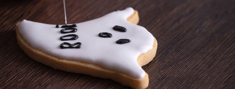 Close up of decorating cute Halloween ghost gingerbread cookies with frosting icing cream topping bag.