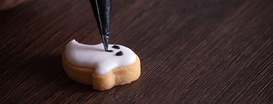 Close up of decorating cute Halloween ghost gingerbread cookies with frosting icing cream topping bag.