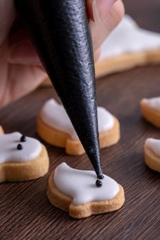 Close up of decorating cute Halloween ghost gingerbread cookies with frosting icing cream topping bag.