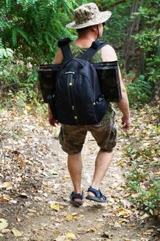a man with a backpack walks along a path in the forest, back view