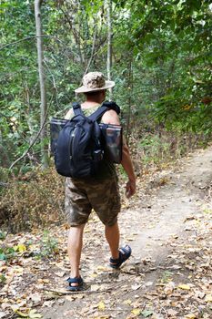 a man with a backpack walks along a path in the forest, back view