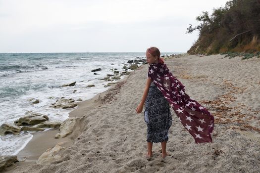 teenage girl with a big scarf walks around the empty beach.