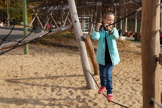 child girl walks the tightrope on the rope playground in the park