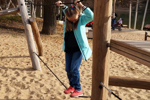 child girl walks the tightrope on the rope playground in the park