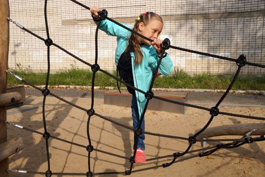 little girl climbing rope ladder on the playground in the park
