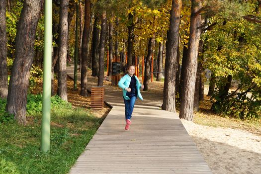 child girl running along the wooden path in the autumn park