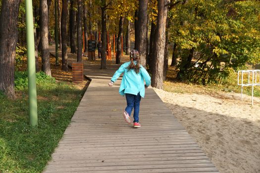 child girl running along the wooden path in the autumn park