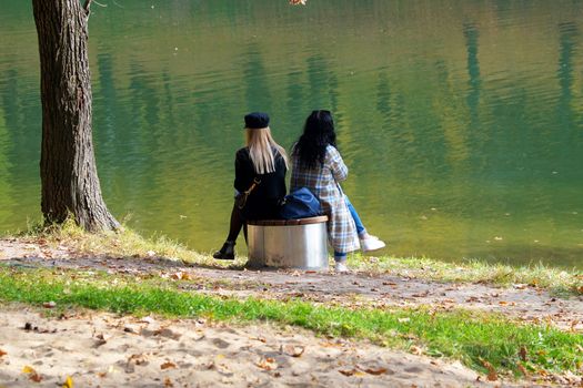 two girls are sitting next to each other on a bench by the lake in an autumn park, LGBT.