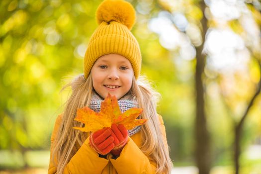 Little girl with blond hair in autumn background in yellow clothing