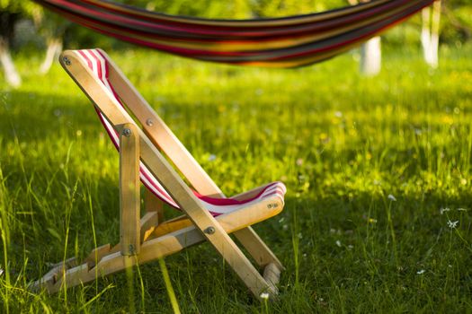 Yard chair on the grass and hammock, summer holiday background. Copy paste space. Sunlight and shadows.