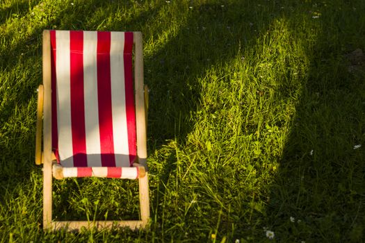 Yard chair on the grass, summer holiday background. Copy paste space. Sunlight and shadows.