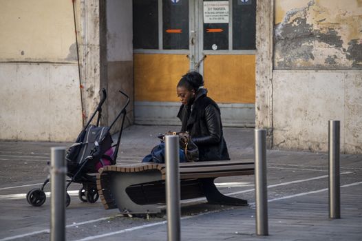 terni,italy october 21 2020:black woman sitting on a bench with a small stroller