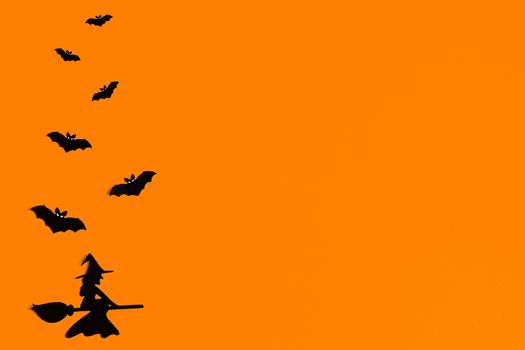 Silhouettes of a flock of bats and a witch flying on a broom made of black paper on an orange background. Halloween greeting template with copy space. Flat lay for your design. ready-made template.