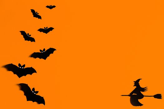 Silhouettes of a flock of bats and a witch flying on a broom made of black paper on an orange background. Halloween greeting template with copy space. Flat lay for your design. ready-made template.