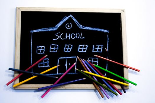 a few colored pencils arranged on a chalkboard where a school building is drawn