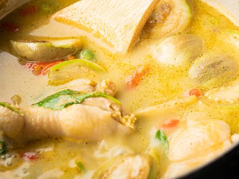Close-up Cooking of Chicken Green Curry, adding Fresh Green Thai Eggplant, Chili and Basil into boiling curry in pan. Local Thai food.