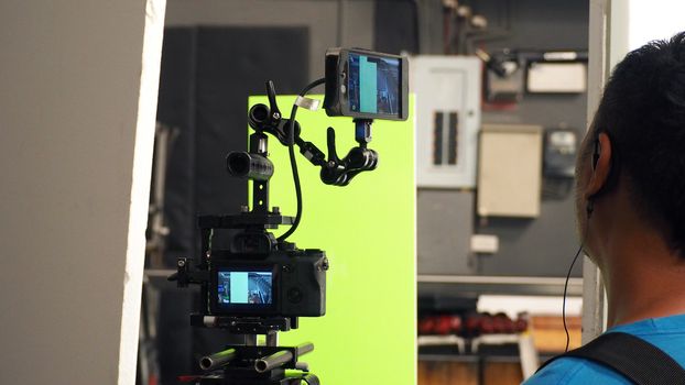 Behind video camera and green screen for movie or film production and equipment in the big studio.