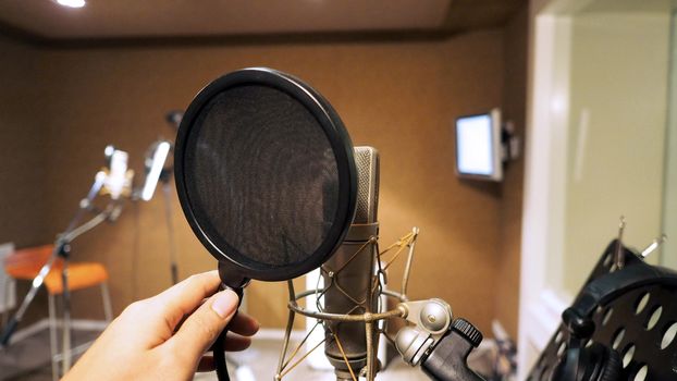 Microphone with shockmount and pop filter on tripod and note stand in recording sound studio video production.