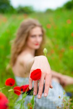 A young long-haired girl enjoys the colors of nature on a blooming poppy field on a hot summer day.