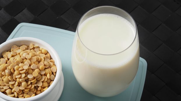 Close-up images of home made healthy drink soy milk with no sugar added in a glass on a green color plastic plate mat and soy beans in small bowl. All of them on black background in a studio shot.