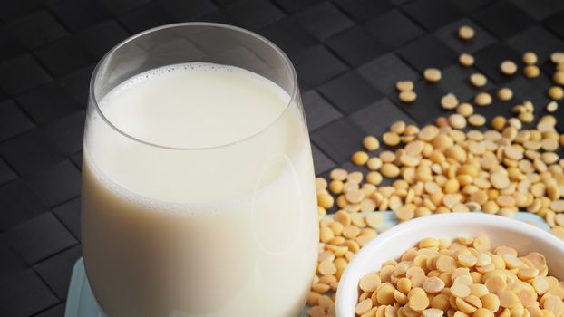 Close-up images of home made healthy drink soy milk with no sugar added in a glass on a green color plastic plate mat and soy beans in small bowl. All of them on black background in a studio shot.