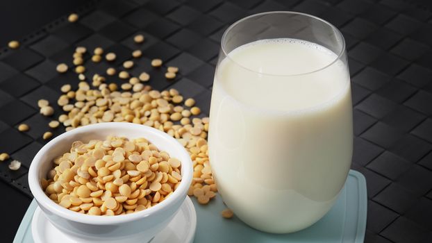 Close-up images of home made healthy drink soy milk with no sugar added in a glass on a green color plastic plate mat and soy beans in small bowl. All of them on black background in a studio shot.