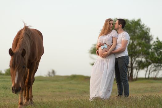 A farmer with his pregnant wife at sunset on his farm. Posing with a horse.