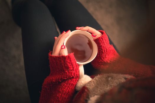 Girl with a warming tea drink in hands sitting on the sofa with christmas colored fingernails