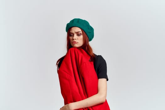 A woman holds in her hand a red coat and a dark T-shirt Green hat cropped view of a light background. High quality photo