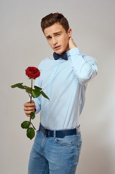 Romantic man with a red rose and in a blue shirt with a bow tie around his neck gray background. High quality photo