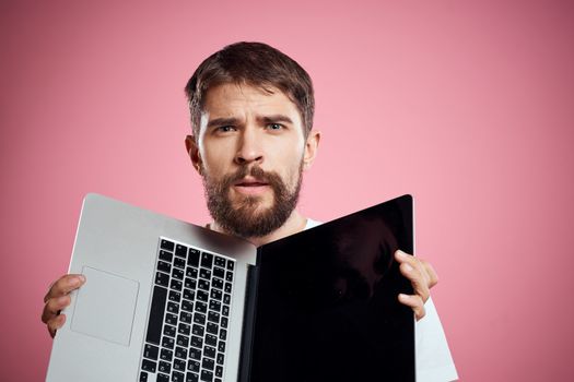 A man with an open laptop on a pink background white t-shirt gestures with his hands cropped view new technology keyboard monitor. High quality photo
