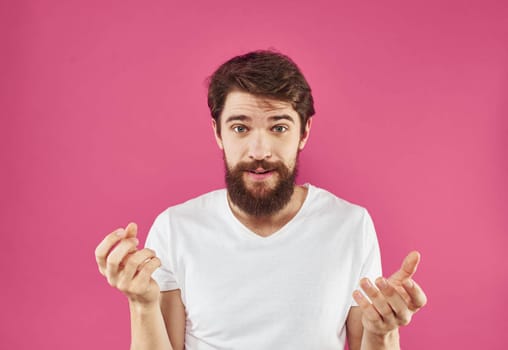 Happy young man on a pink background in a white T-shirt and a thick beard gesticulate with his hands. High quality photo