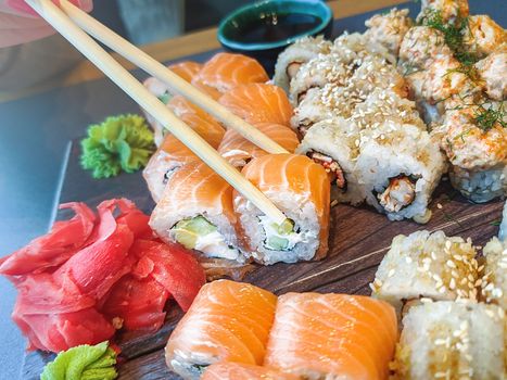 Girl's hand holding chopsticks and eating various sushi rolls in restaurant.