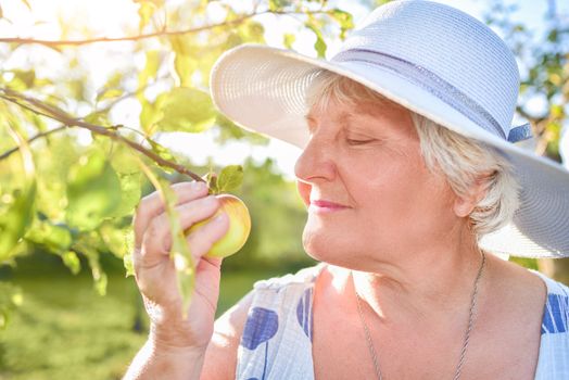 Happy senior woman blooming and enjoying flowers in the garden under apple tree