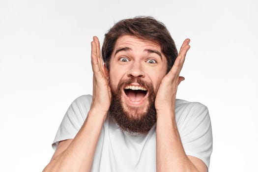 cheerful bearded man in a white t-shirt emotions gestures with his hands light background studio. High quality photo