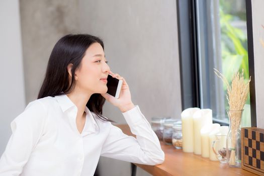 Beautiful young asian woman talking phone and smile in the coffee shop, businesswoman sitting in cafe free time, freelancer female calling telephone, communication concept.