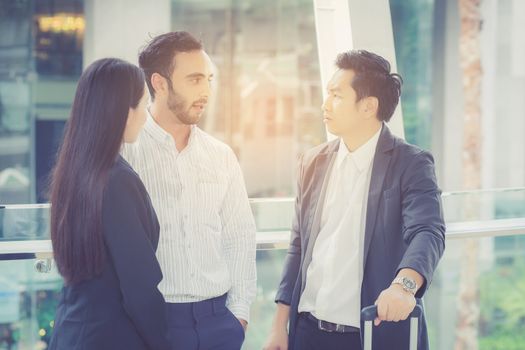 handsome asian young businessman and businesswoman three people in classic suits talking and smile with discussion standing outside the office building, teamwork with business concept.