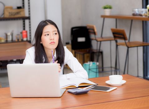 Asian young woman working online with laptop and think project for idea at modern cafe shop, business and freelance concept.