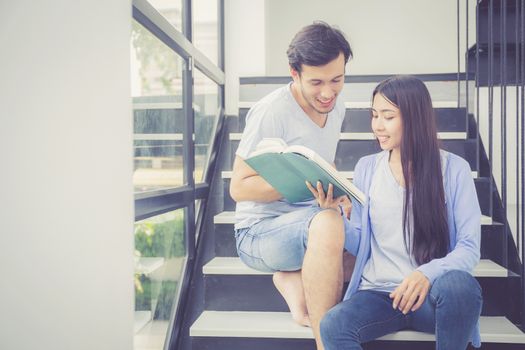 Couple asian handsome man and beautiful woman reading book and smile at home, boyfriend and girlfriend with activities together for leisure, education concept.