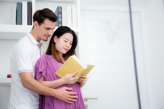 Husband with pregnant woman reading yellow book together, Portrait of couple with hug, happy with family choose name newborn concept.