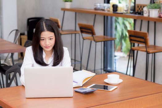 Beautiful asian young woman working online on laptop sitting at coffee shop, professional female freelancer using notebook computer with connect to internet for distance job.