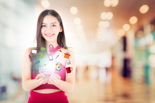 Beautiful asian young woman in red dress holding shopping cart with icon product on blur bokeh background, ecommerce shopping online concept.