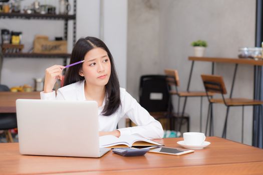 Asian young woman working online with laptop and think project for idea at modern cafe shop, business and freelance concept.