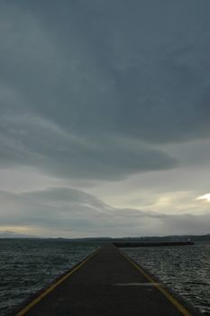 Long jetty path leads to the grey stormy ocean in evening