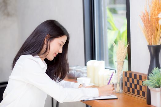 Beautiful business asian young woman writing on notebook on table, girl work at coffee shop, freelance business concept.